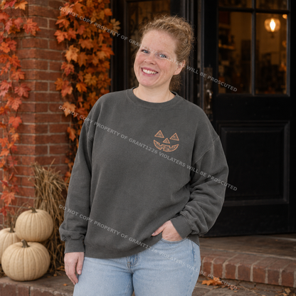 Woman wearing pepper Comfort Colors geometric jack-o-lantern embroidered sweatshirt outside a brick storefront
