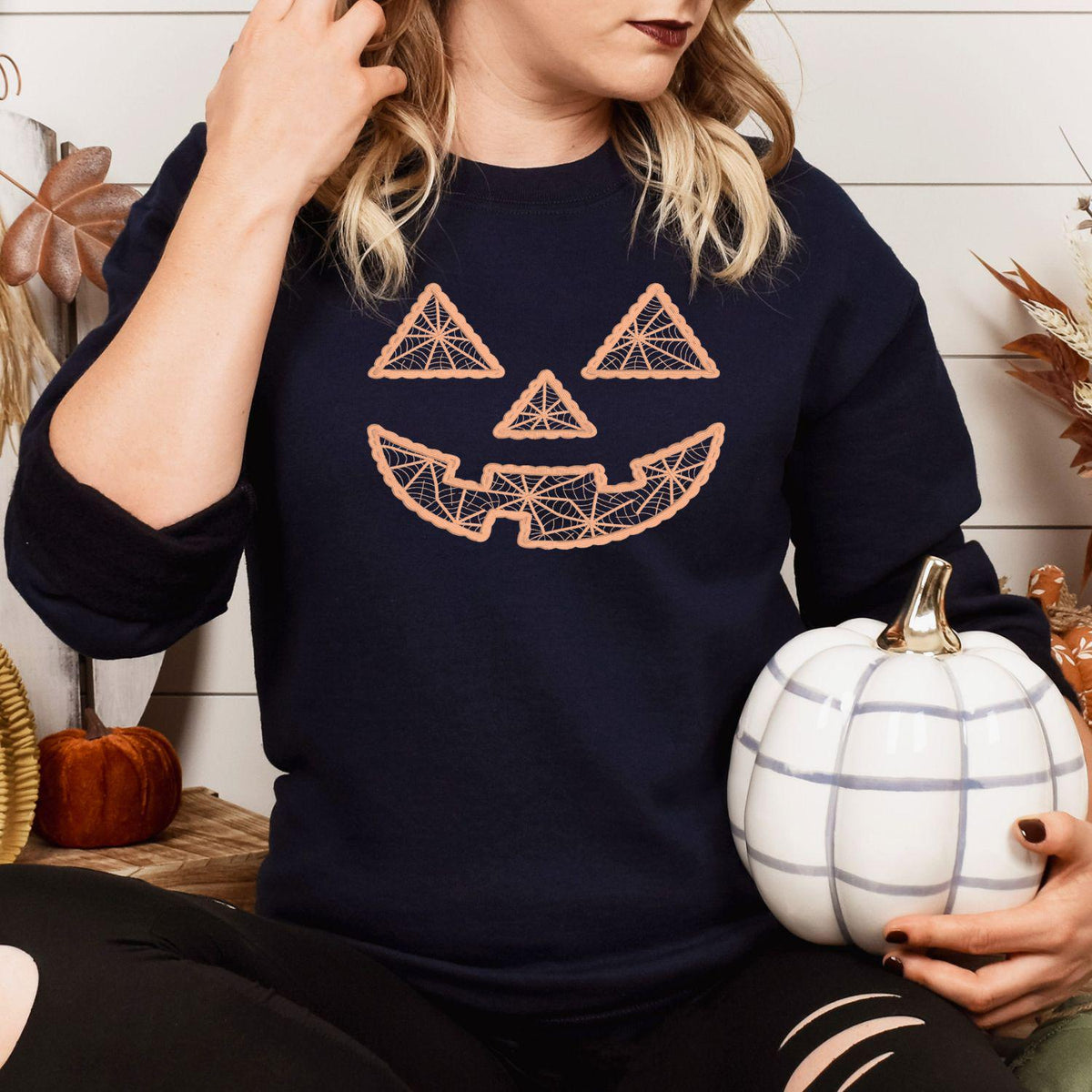 Model wearing navy sweatshirt with geometric jack-o-lantern face embroidery