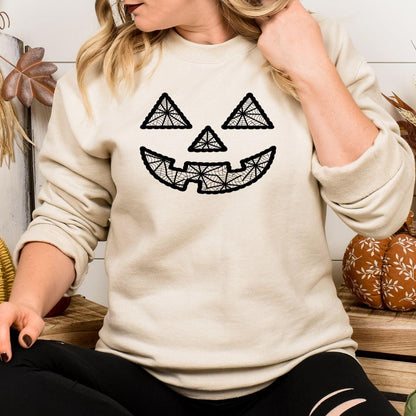 Model wearing sand sweatshirt with black geometric pumpkin face embroidery