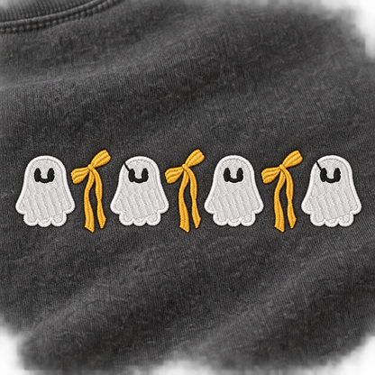 Close-up of four white ghosts and three golden bows embroidered on Pepper sweatshirt fleece