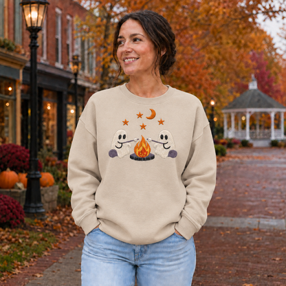 Adult wearing a Sand embroidered ghost campfire sweatshirt with two ghosts roasting marshmallows