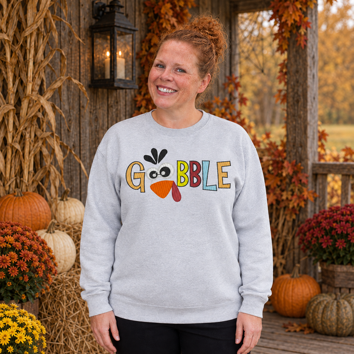 Samantha wearing a Sport Grey Gobble turkey embroidered Thanksgiving sweatshirt on a rustic fall porch