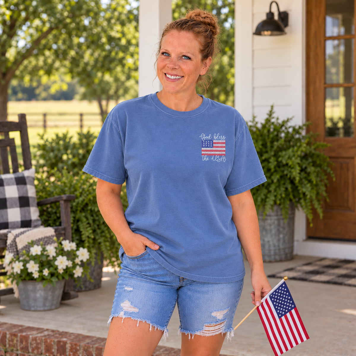 Samantha wearing a Blue Jean Comfort Colors tee with God Bless the USA left-chest embroidery and holding a small American flag