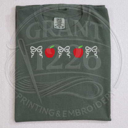 Folded moss green teacher shirt with embroidered apple and bow design