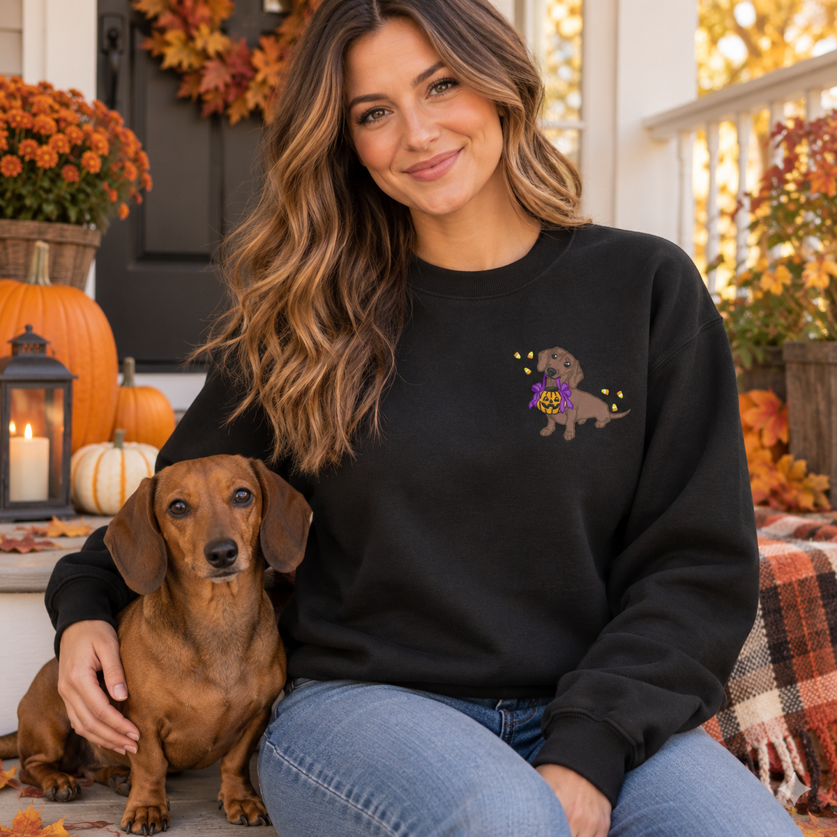 Woman wearing black Halloween dachshund embroidered sweatshirt with a brown dachshund on an autumn porch
