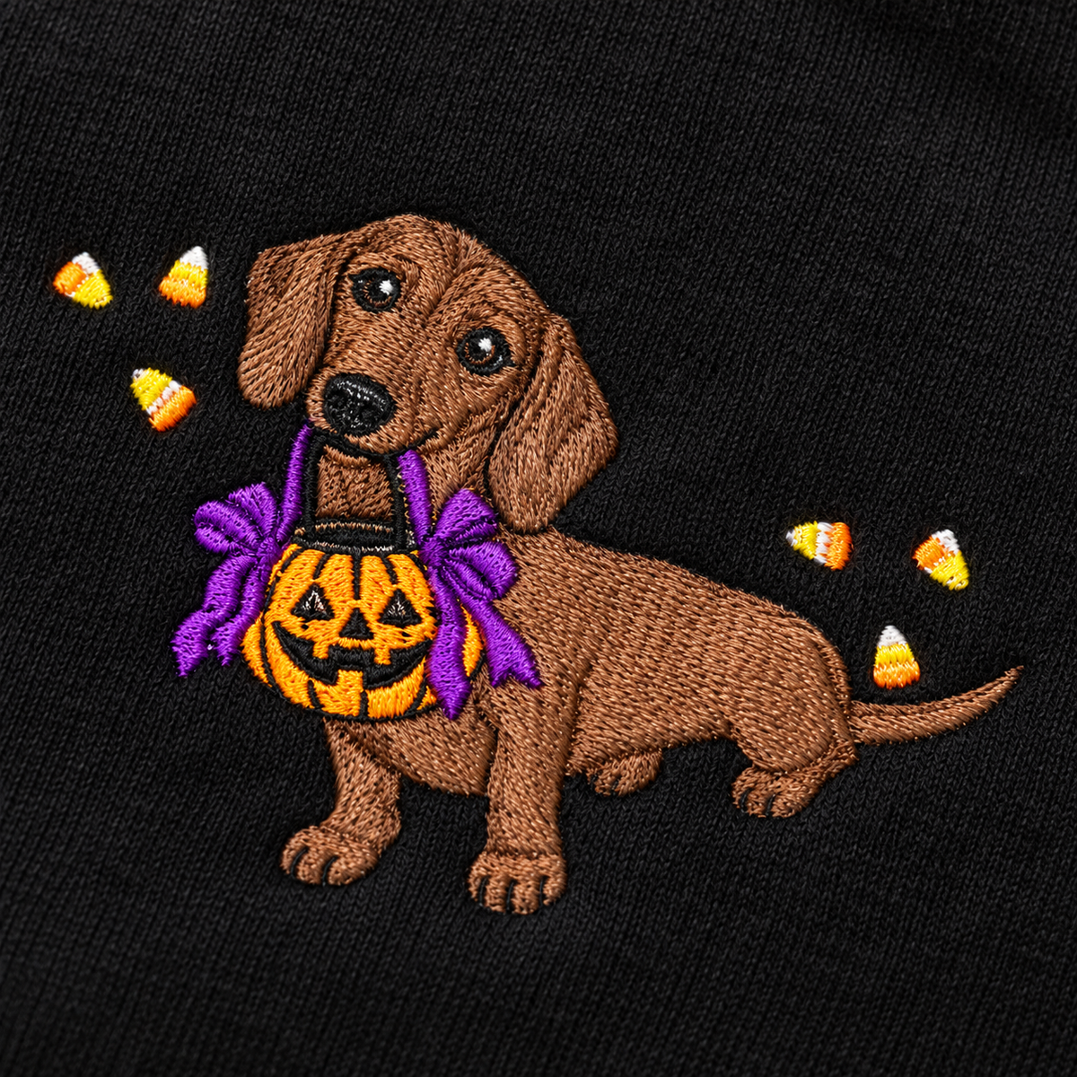 Close-up of dachshund, pumpkin bucket, purple bows and candy corn embroidery stitched on black sweatshirt fabric