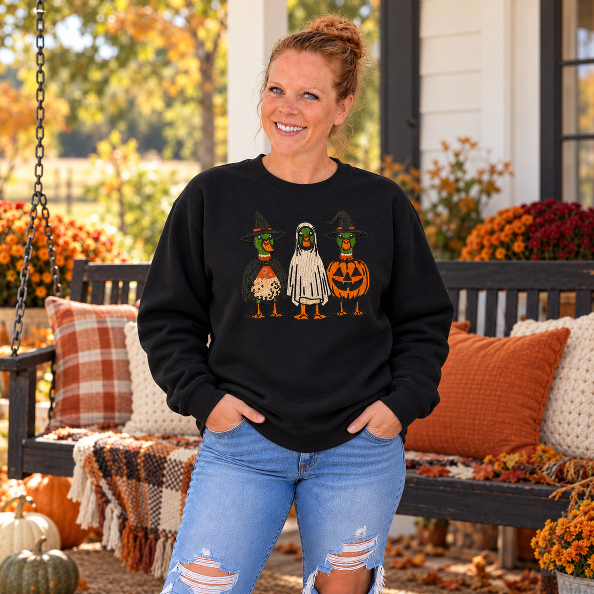 Woman wearing Black Halloween Duck embroidered sweatshirt by a fall porch swing