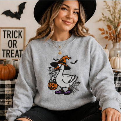 Woman wearing grey embroidered Halloween goose sweatshirt with witch hat, pumpkin bucket, bats and spiderwebs