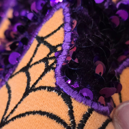 Macro detail of Halloween MAMA sequin appliqué stitching beside the embroidered spiderweb