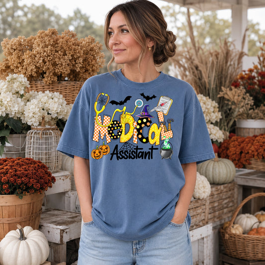 Woman wearing a Blue Jean Comfort Colors Halloween Medical Assistant shirt with pumpkins, bats and stethoscope.