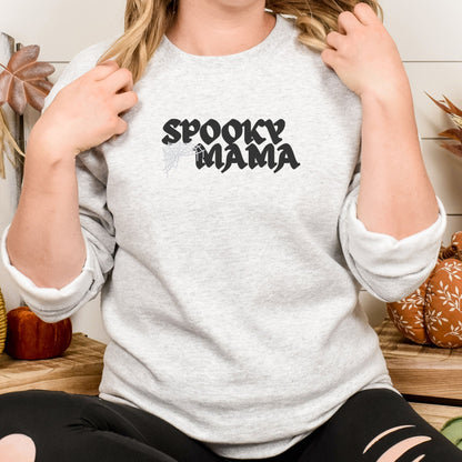 Woman wearing ash gray Halloween Mama embroidered crewneck with black Spooky Mama lettering and spiderweb