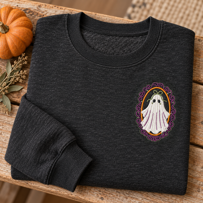 Folded heathered-black ghost sweatshirt on a rustic bench with a pumpkin and dried sage.