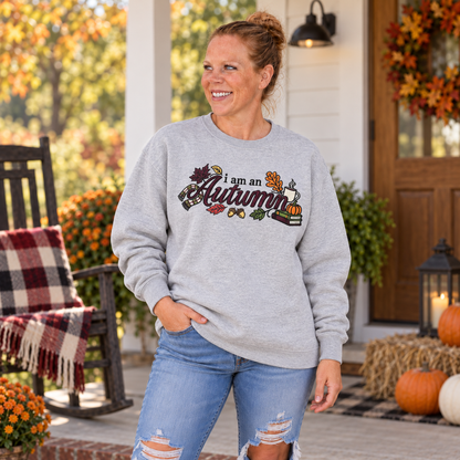 Woman wearing Sport Grey embroidered I Am an Autumn Gildan Softstyle sweatshirt on a fall porch