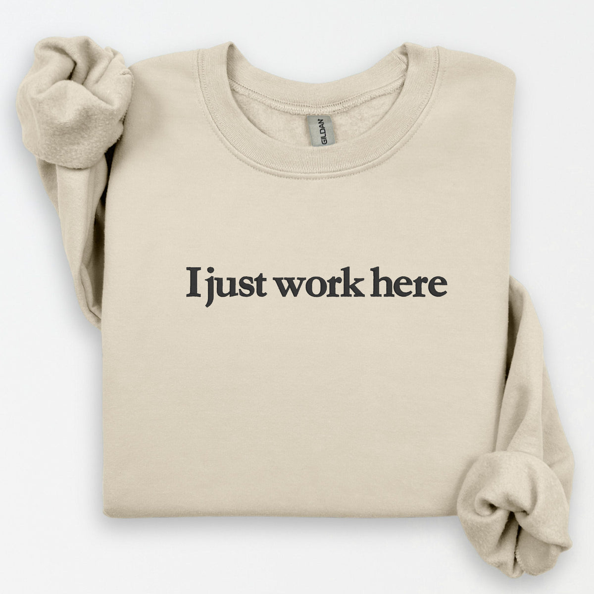 Sand Gildan crewneck sweatshirt embroidered with I Just Work Here in a flat-lay product view