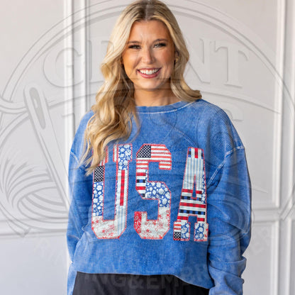 Model wearing blue oversized USA applique corded sweatshirt with red white and blue patriotic patchwork letters.