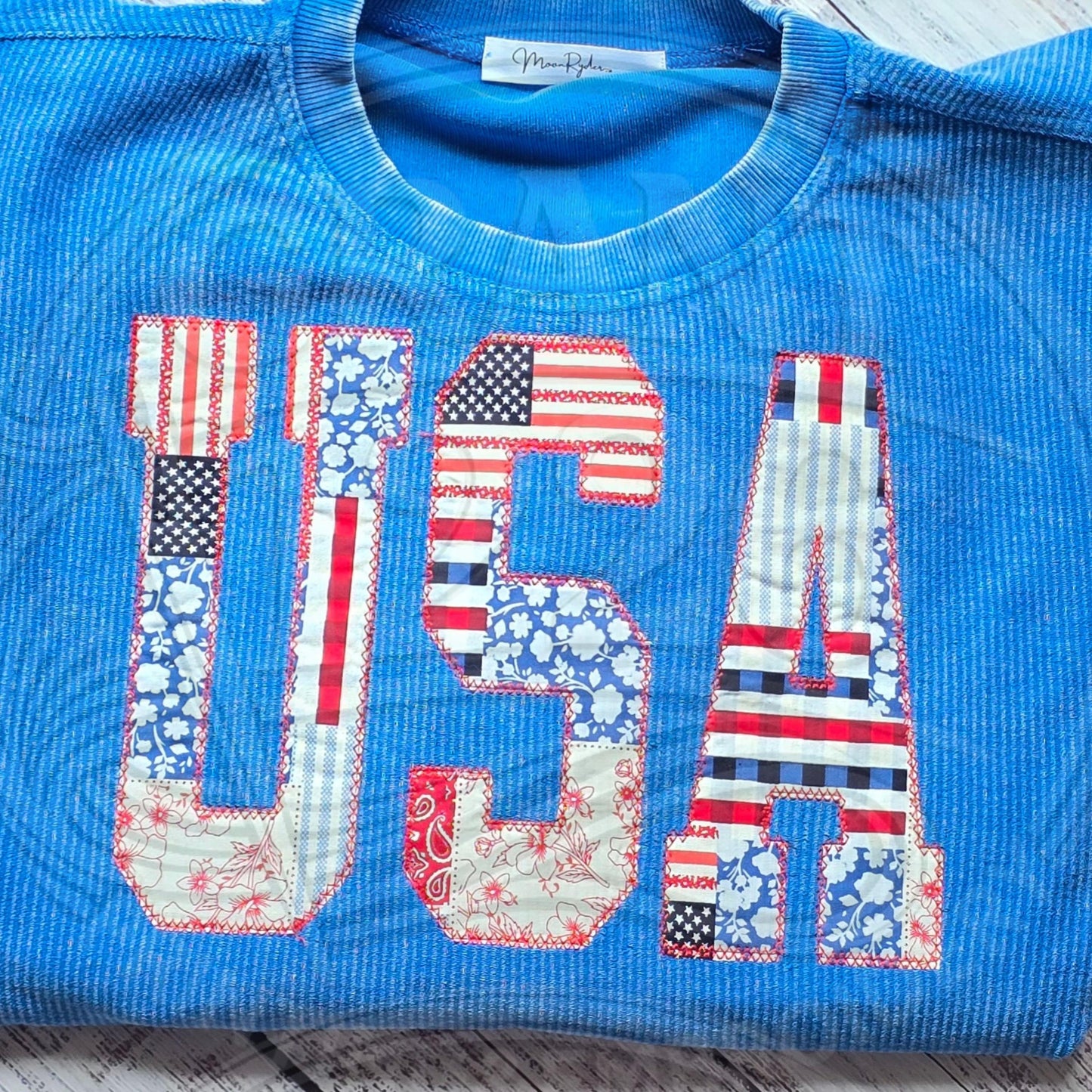 Blue corded sweatshirt with red white and blue USA patchwork applique letters stitched across the front.