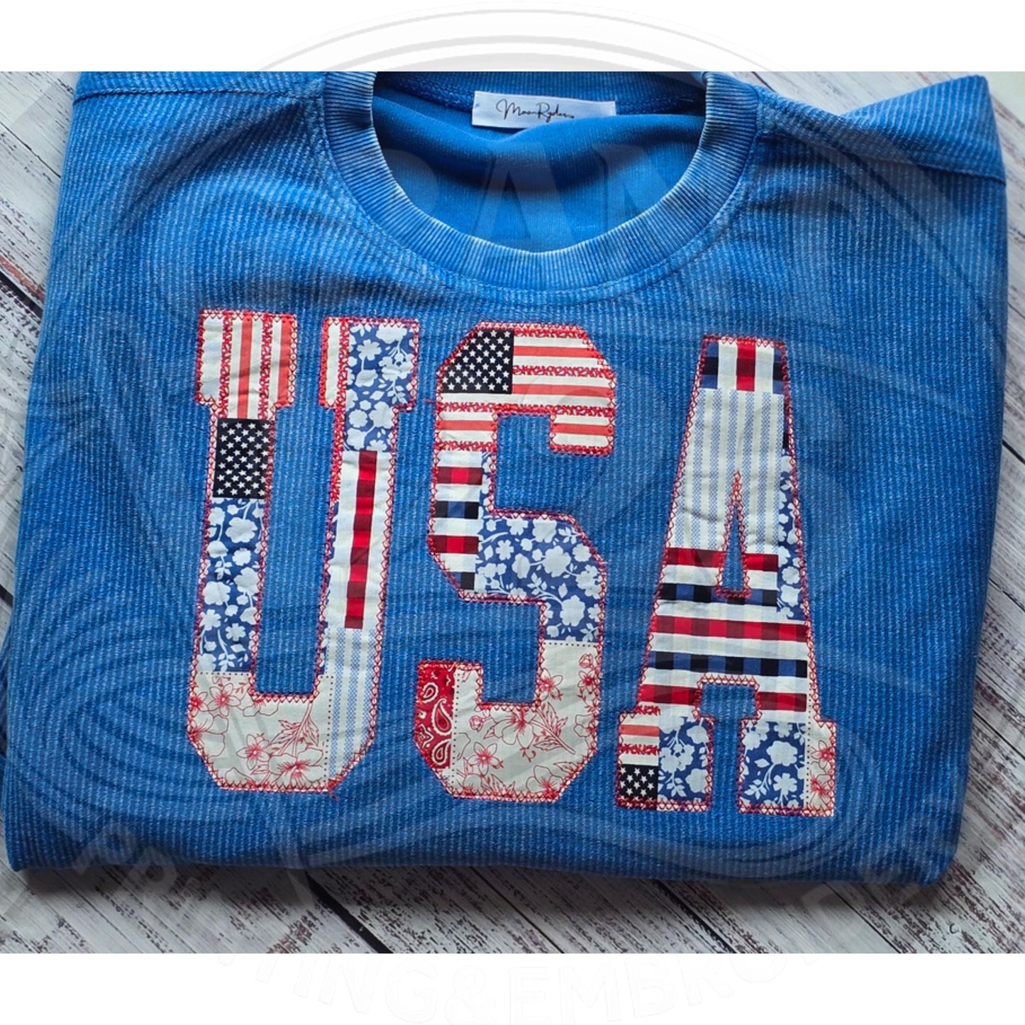 Patriotic USA applique sweatshirt in bright blue corded fabric shown folded with red white and blue patchwork letters.