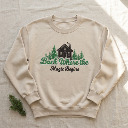 Sand crewneck sweatshirt flat-lay mockup with cabin, evergreen trees, and Back Where the Magic Begins embroidery