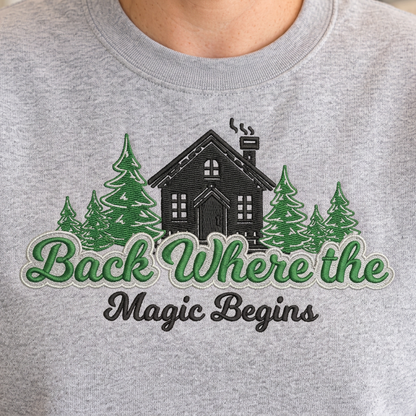 Sport Grey sweatshirt mockup showing close-up cabin and evergreen embroidery with Back Where the Magic Begins lettering