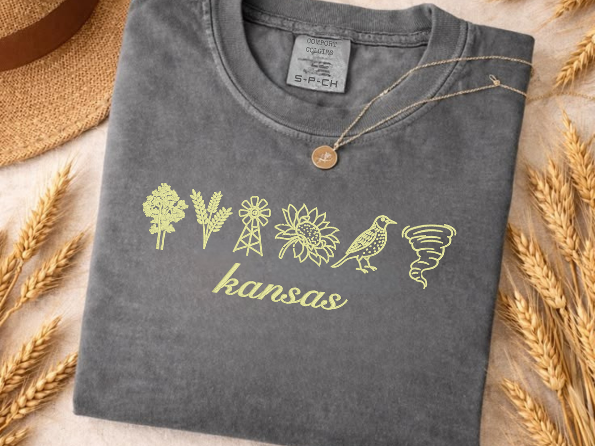 Close-up of Kansas symbols embroidered in yellow on a charcoal Comfort Colors shirt