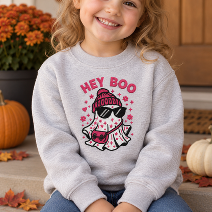 Child wearing an ash sweatshirt with centered pink and black Hey Boo ghost embroidery
