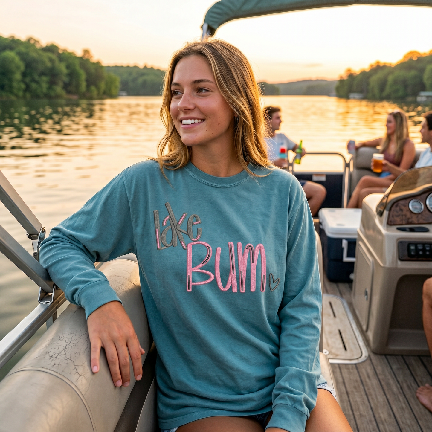 Woman wearing blue embroidered Lake Bum long sleeve shirt relaxing on pontoon boat