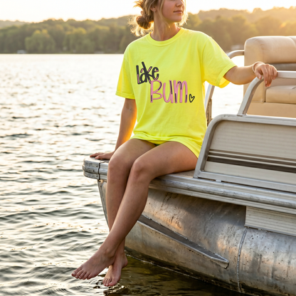 Woman sitting on pontoon boat wearing neon yellow embroidered Lake Bum summer shirt
