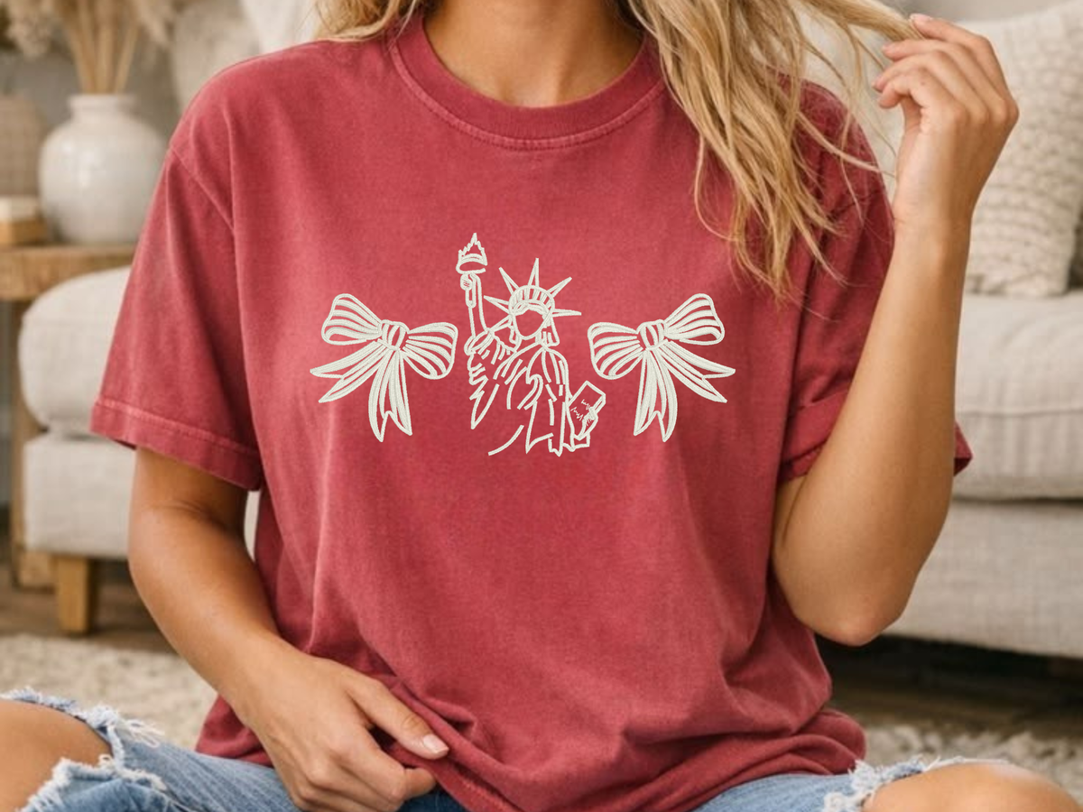 Red Comfort Colors shirt modeled with an embroidered Statue of Liberty and bow design
