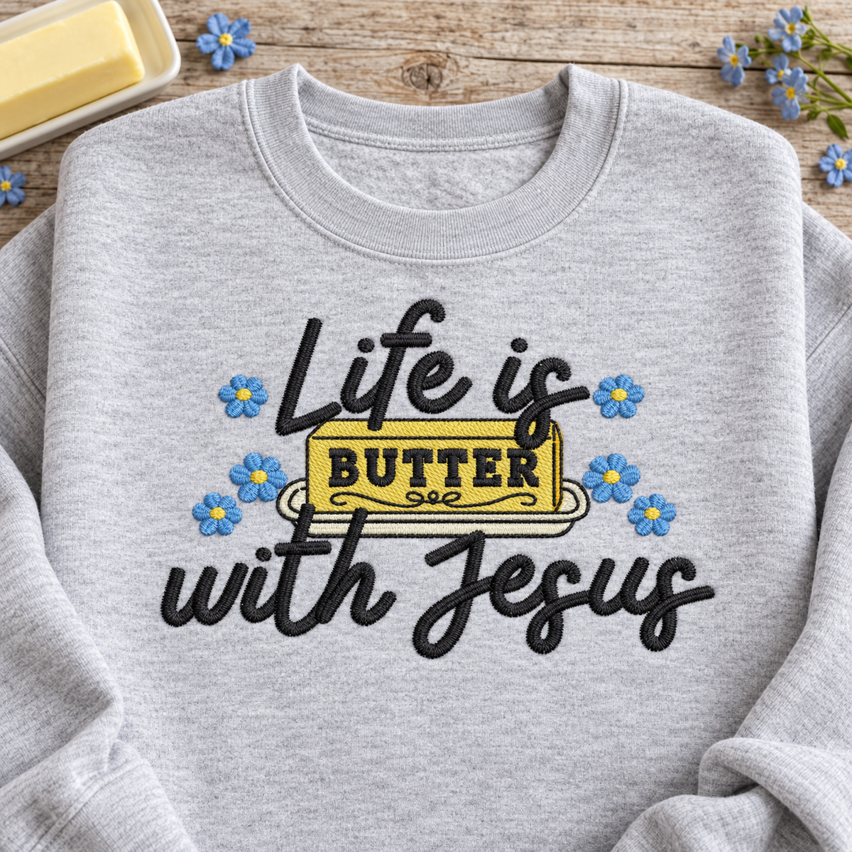 Close-up of Life Is Butter With Jesus embroidery with yellow butter and blue flowers
