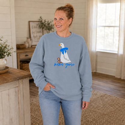 Woman wearing a dusty blue crewneck embroidered with a white goose, blue bow, and Mama Goose lettering.