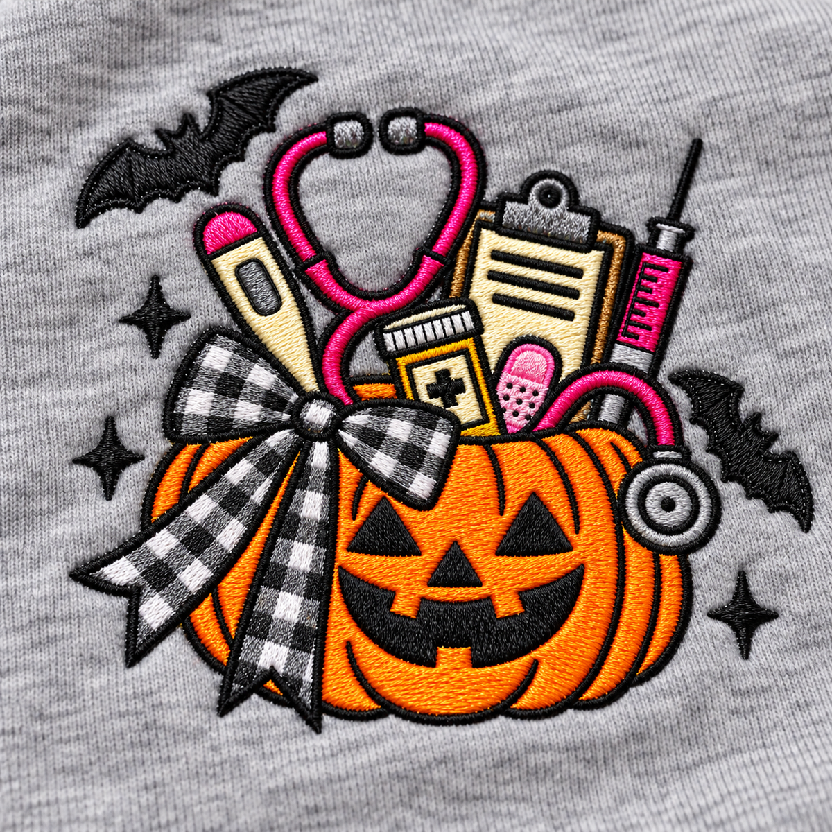 Close-up of orange medical pumpkin embroidery with pink stethoscope, gingham bow, bats and medical tools
