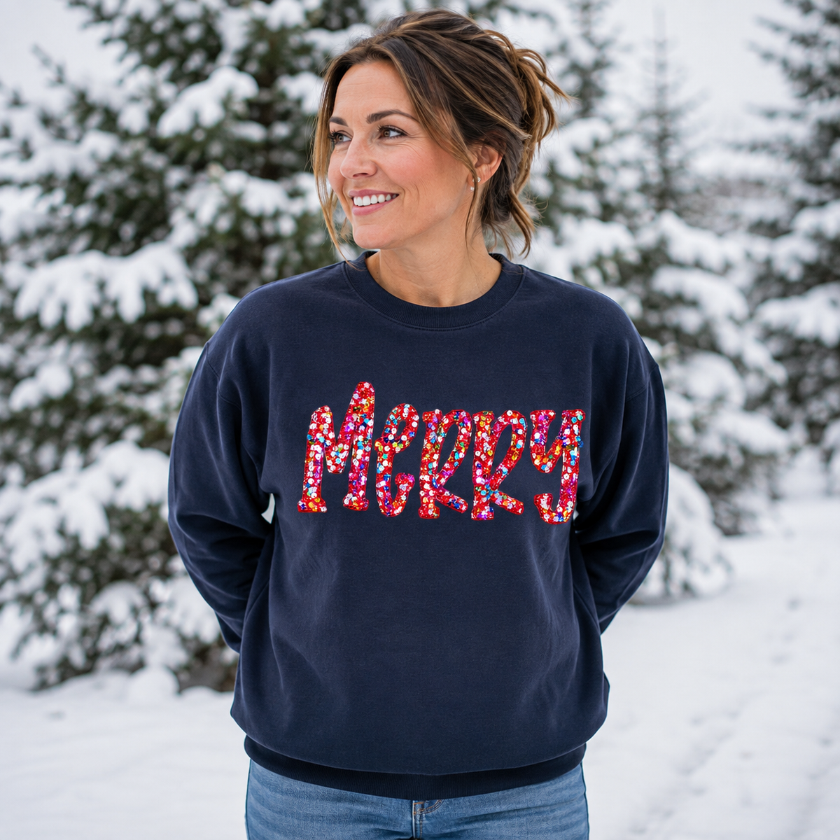 Mockup of a woman wearing a navy MERRY sweatshirt with multicolored sequin lettering outdoors in snow