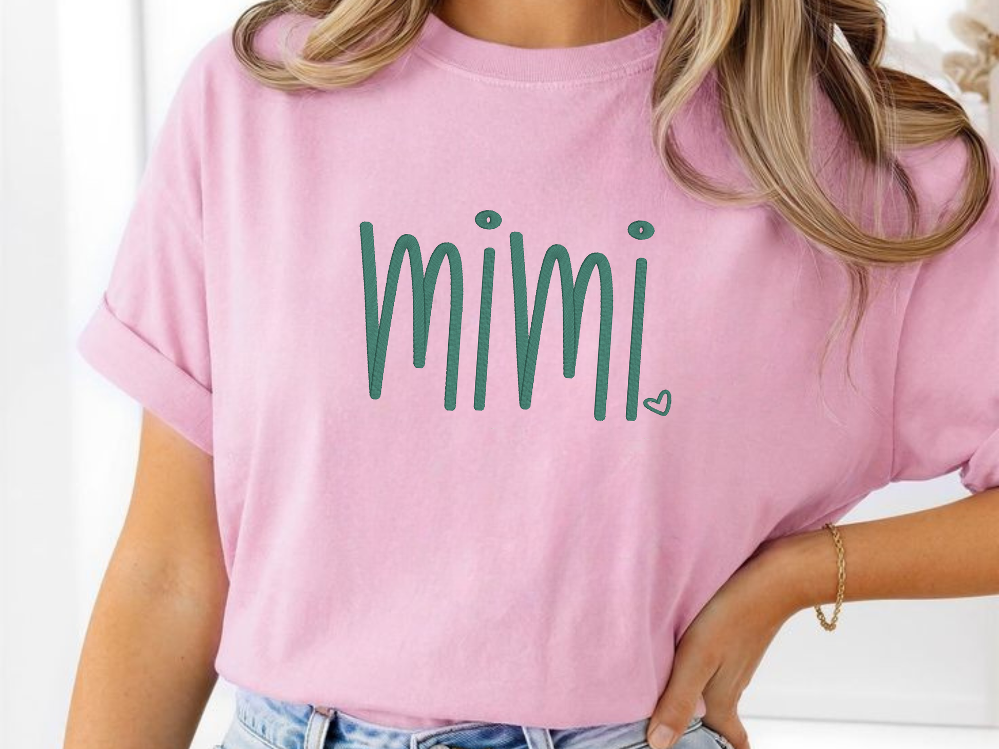 Person wearing a pink t-shirt with 'mimi' embroidered in green.