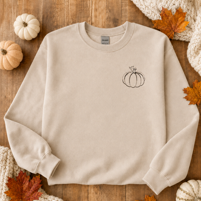 Sand Gildan Softstyle sweatshirt flat lay with small black pumpkin embroidery and autumn leaves
