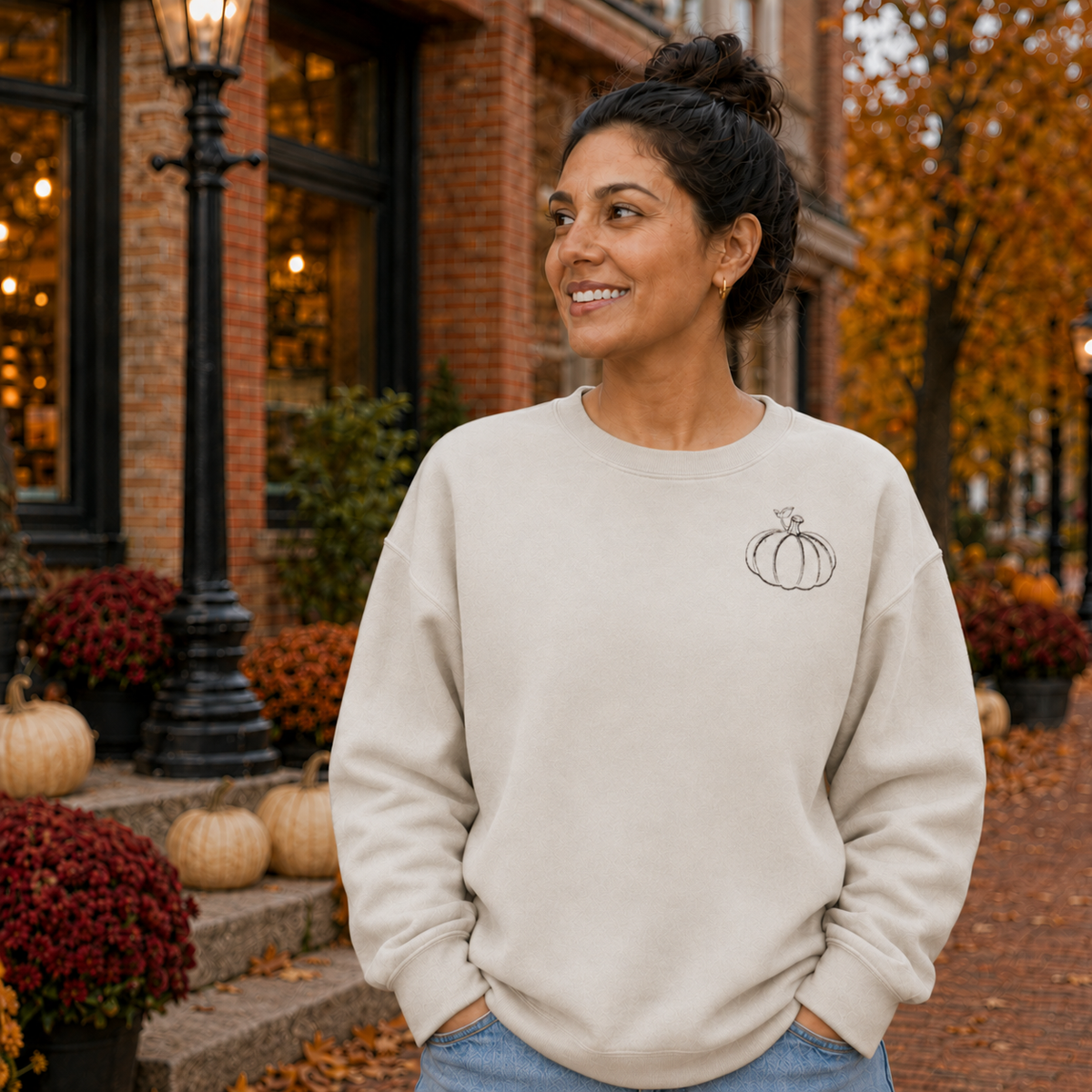 Sand Gildan Softstyle sweatshirt with small black pumpkin embroidery in an autumn town setting