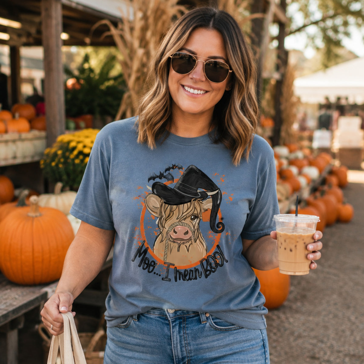 Woman wearing a Blue Jean Comfort Colors Highland cow witch Halloween shirt at a pumpkin patch