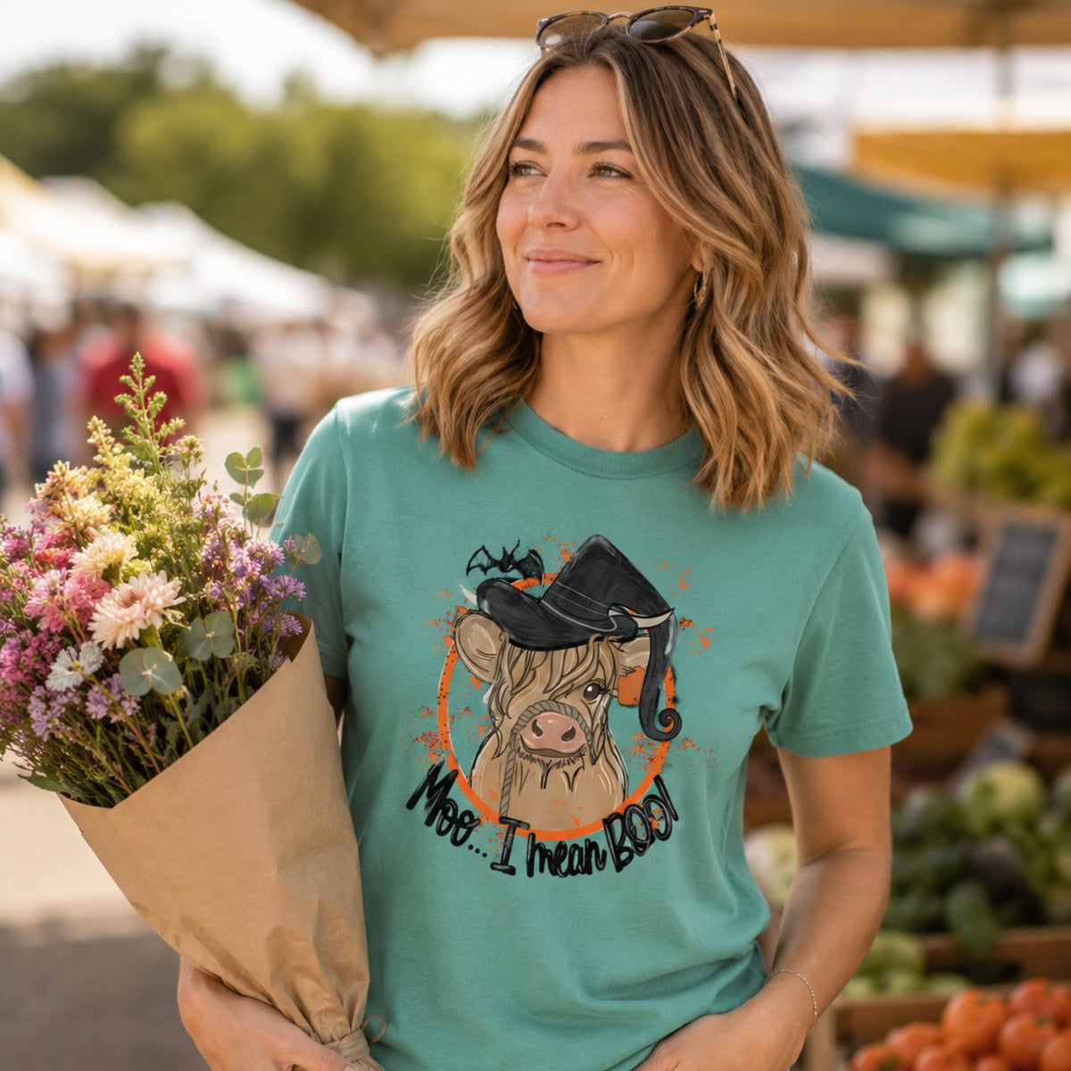 Woman wearing a Seafoam Comfort Colors Highland cow witch Halloween shirt at a fall market