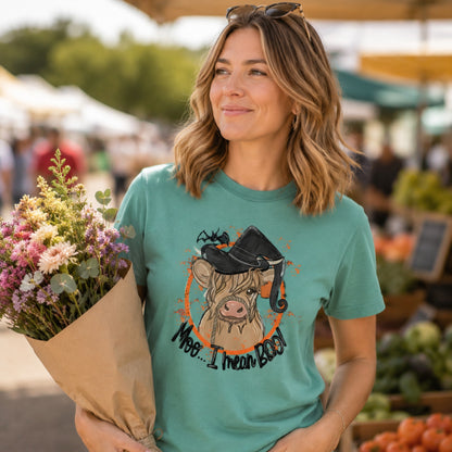 Woman wearing a Seafoam Comfort Colors Highland cow witch Halloween shirt at a fall market