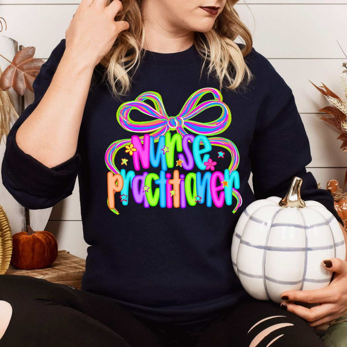 Model wearing navy Nurse Practitioner bow sweatshirt with fall pumpkins