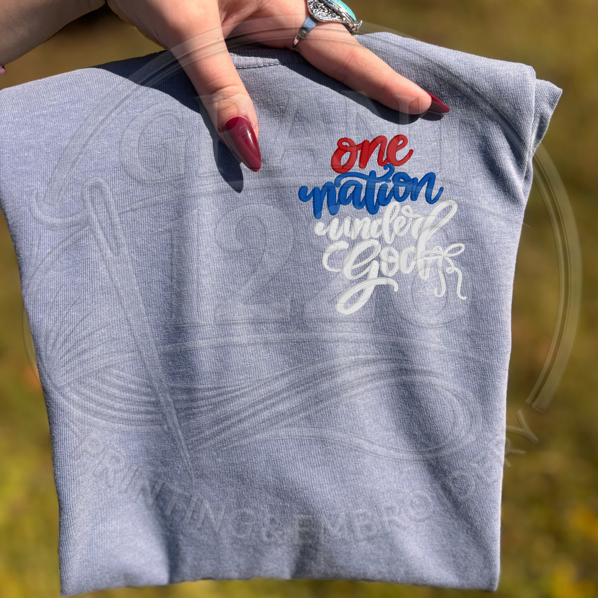 Gray One Nation Under God embroidered shirt held outdoors