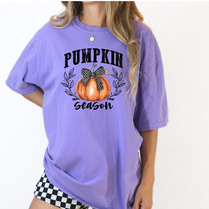Orchid Comfort Colors Pumpkin Season shirt with orange pumpkin, polka-dot bow, and leafy fall design.