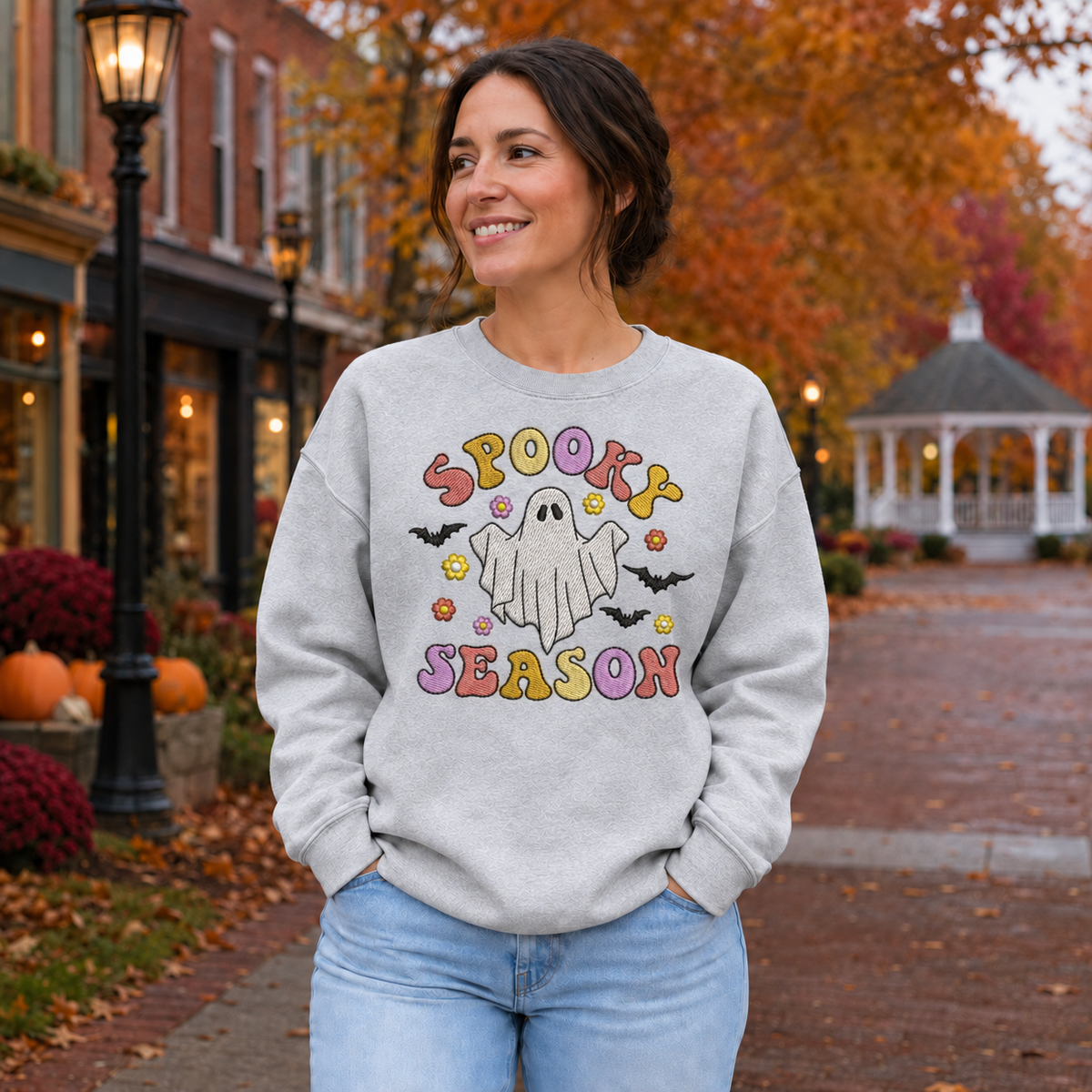 Woman wearing a Sport Grey pastel Spooky Season ghost embroidered sweatshirt in an autumn town