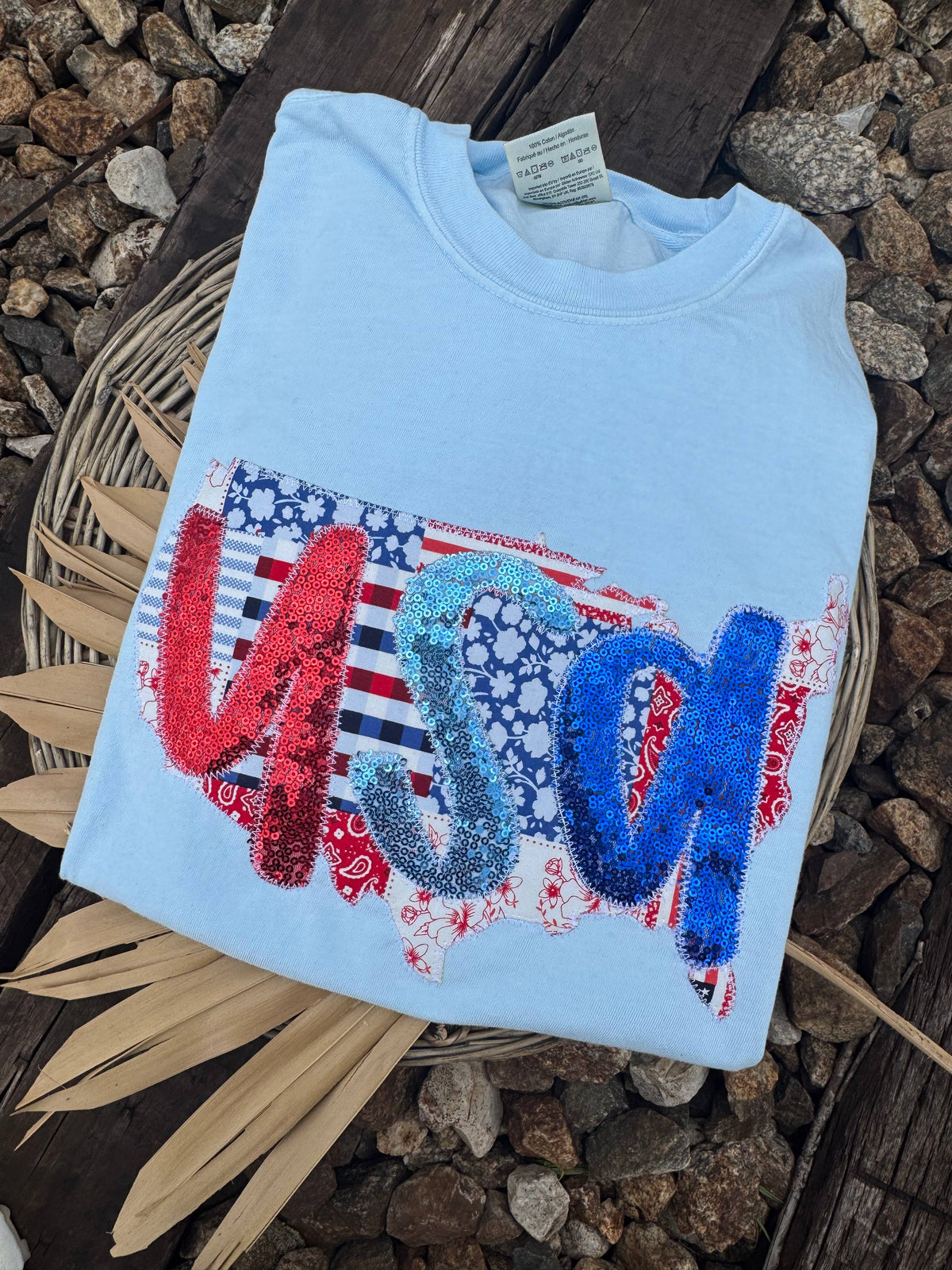 Light blue shirt with a red white and blue patchwork USA design displayed on rocks
