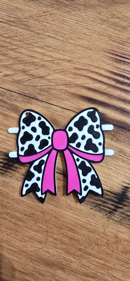 3D printed pink cow-print bow hair tie holder on a wood background