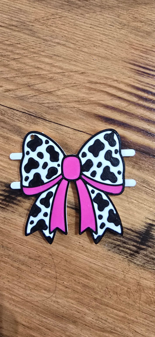 3D printed pink cow-print bow hair tie holder on a wood background