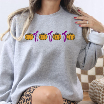 Ash Gildan 18000 sweatshirt with embroidered orange pumpkins and pink bows in a fall lifestyle setting