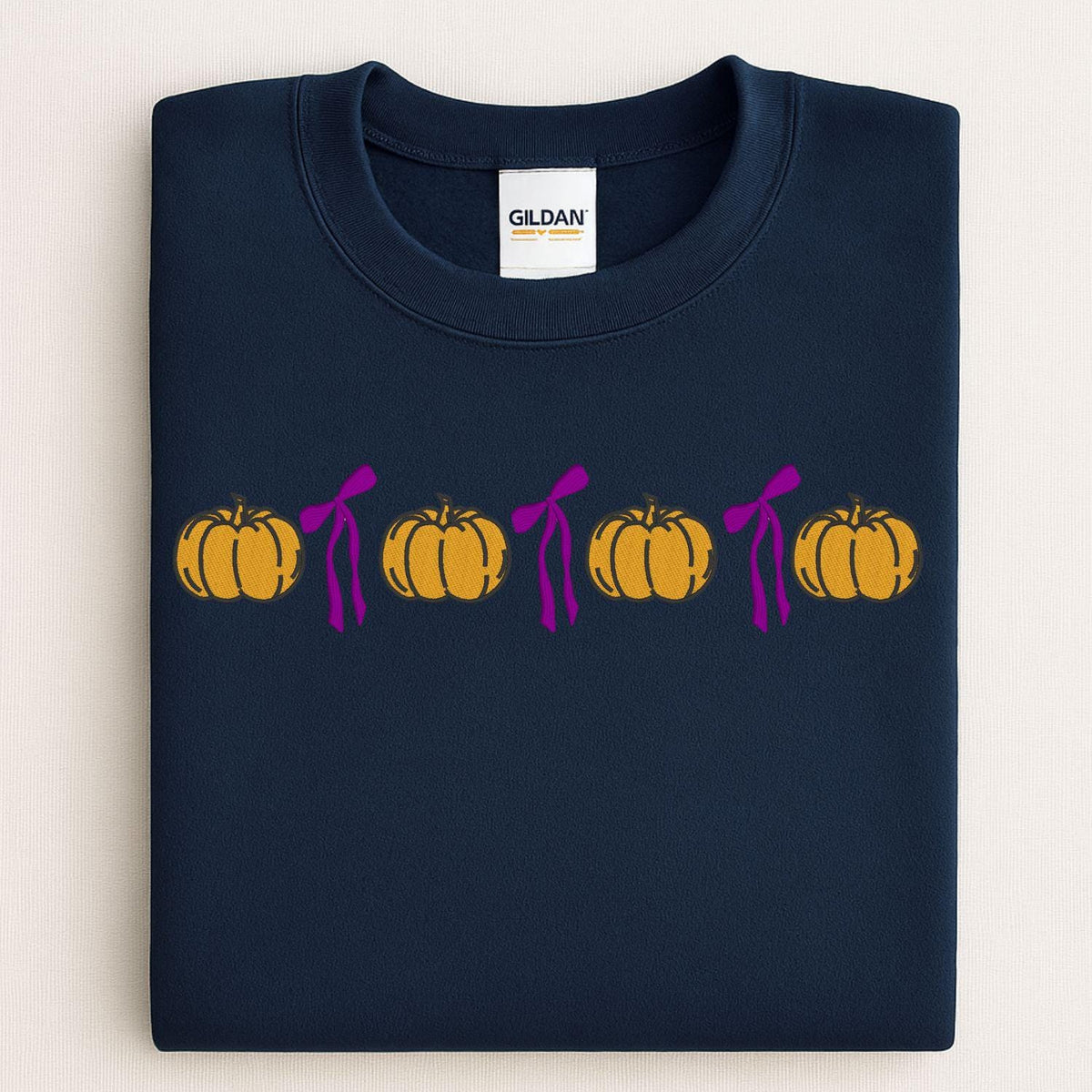 Folded Navy Gildan sweatshirt with a row of embroidered pumpkins and pink bows