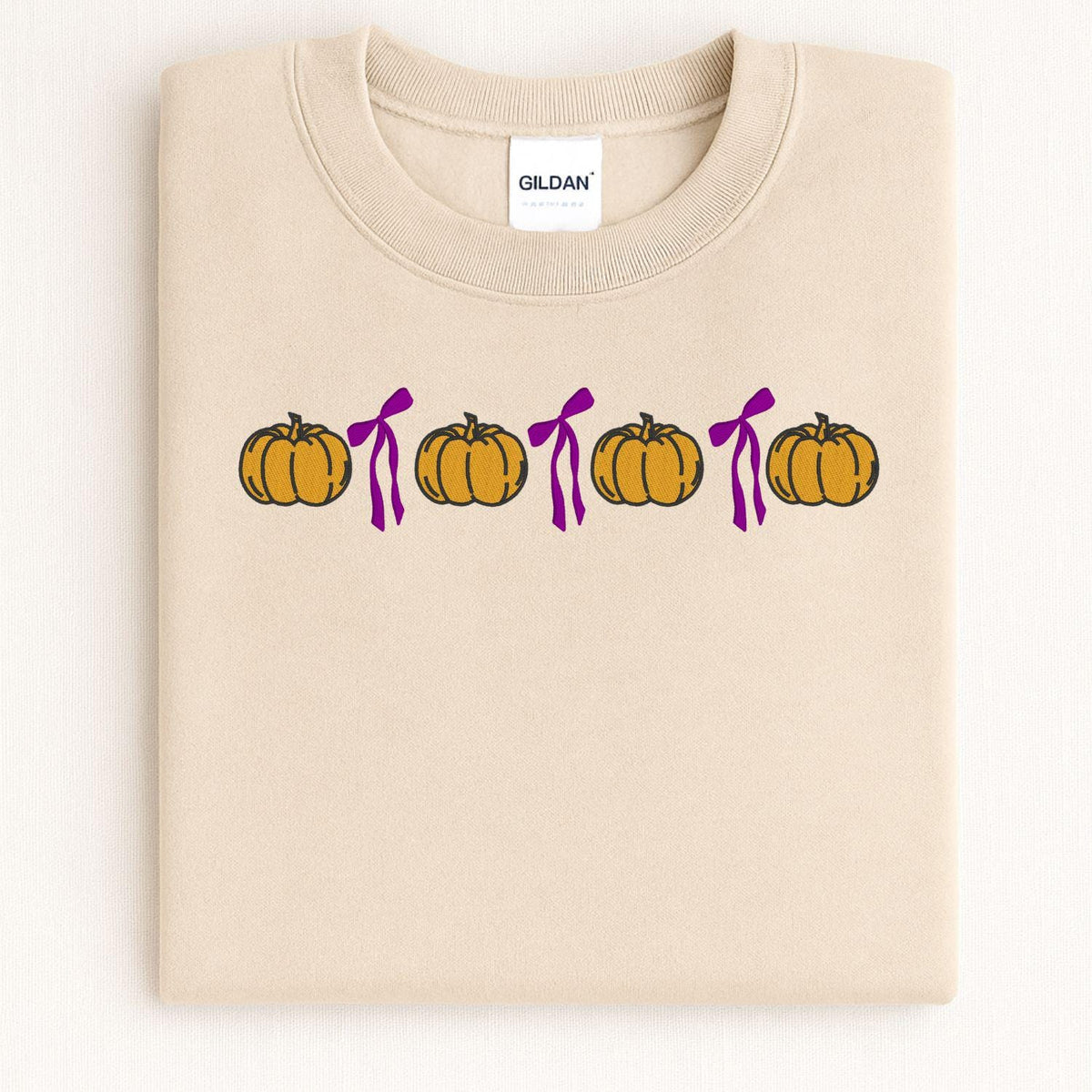 Folded Sand Gildan sweatshirt with orange pumpkin and pink bow embroidery