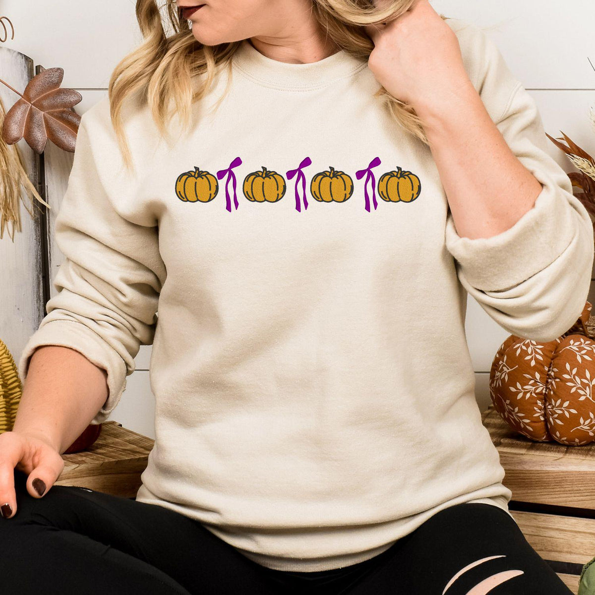 Sand Gildan 18000 sweatshirt with embroidered orange pumpkins and pink bows in a fall lifestyle setting