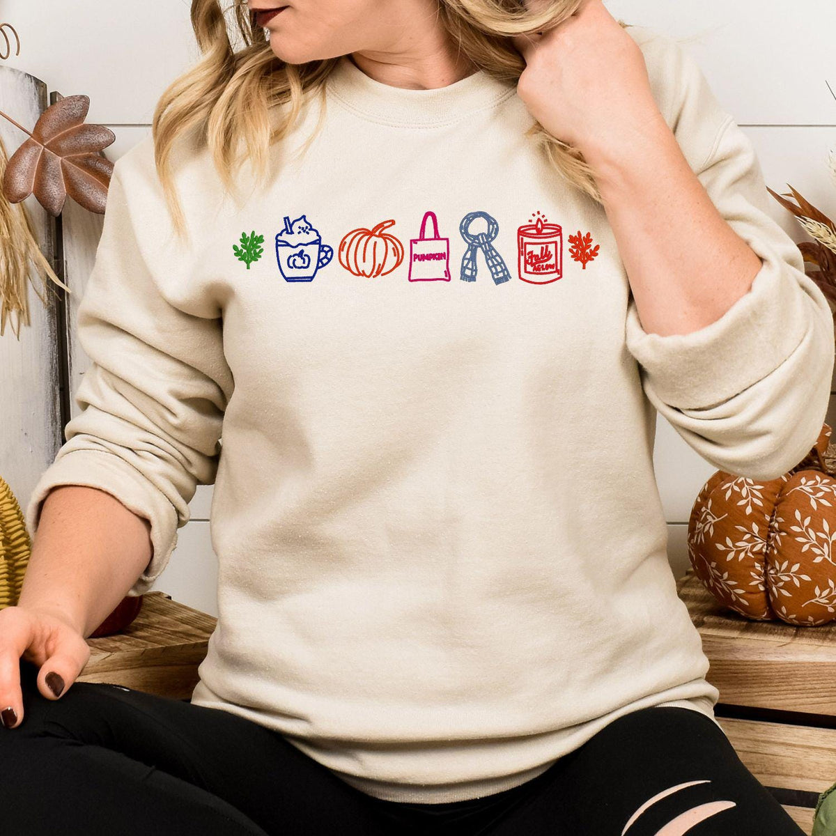 Sand sweatshirt with a colorful row of embroidered fall icons modeled indoors